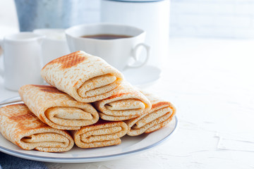 Homemade pancakes stuffed, wrapped with an envelope on a white plate, traditional food on a pancake week, horizontal, copy space
