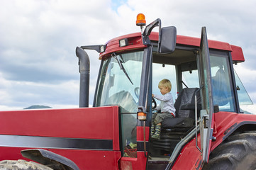 Little blond boy playing in tractor, outdoors