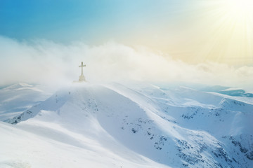 Fototapeta na wymiar Mountain peaks covered by snow and Heroes cross on top of Bucegi illuminated by sunset light in winter season