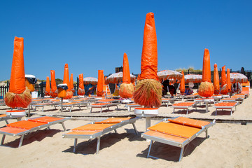 Empty beach with orange sun loungers and closed umbrellas