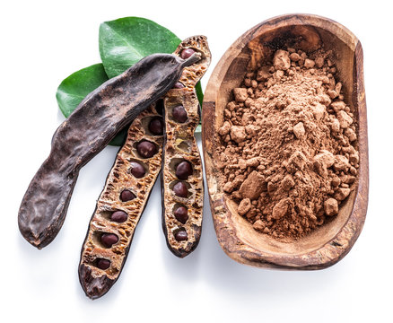 Carob pods and carob powder in the wooden bowl.