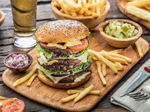 Big hamburger and French fries on the wooden tray.