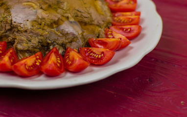 A jellied meat in a round plate decorated with tomatoes on a wooden surface of a color tawny port.