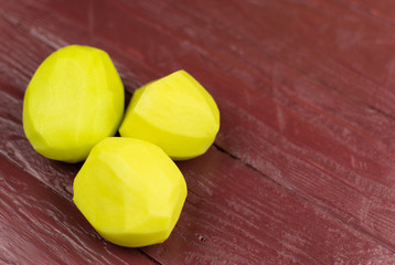Peeled potatoes on a dark red wood background.