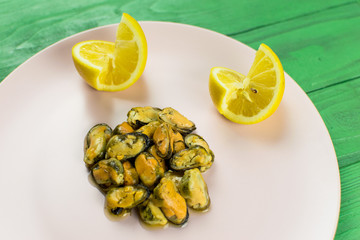 Mussels on a pink-lilac-colored plate on a wooden green background.