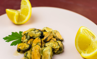 Mussels on a pink-lilac-colored plate on a wooden dark red background.
