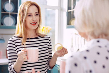 Nice morning. The focus being on a pleasant young woman talking to her beloved elderly mother and smiling at her while drinking coffee together in the kitchen in the morning