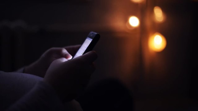 Pregnant woman using mobile phone in dark room, close up of hands typing text message on smart phone