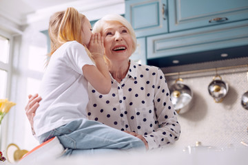 Our little secret. Pleasant charming elderly woman hugging her little granddaughter and listening...