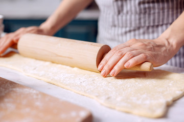 Best skills. The close up of delicate female hands using a rolling spin and rolling out dough on the kitchen counter while making biscuits