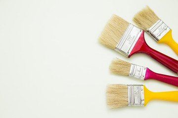 Fototapeta premium Painting the house. Two red and two yellow paint brushes on white background with copy space, top view, flat lay