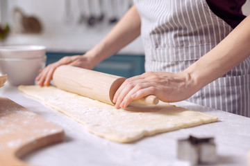 Obraz na płótnie Canvas Cooking skills. The focus being on the delicate hands of a young woman wearing an apron and using a rolling spin to roll out dough on the kitchen counter