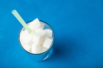 Close-up, a glass with sugar cubes on a blue background. The amount of sugar in sweet soda or juice. Copy space.