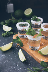 Alcohol shots on wooden tray. Shooter glasses of vodka or Tequila on black table. Mojito with mint