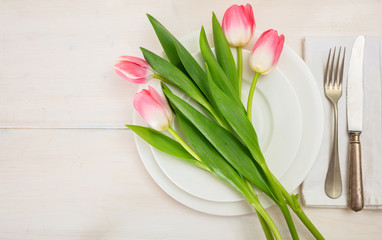 Spring table setting with pink tulips on white wooden background. Top view, copy space