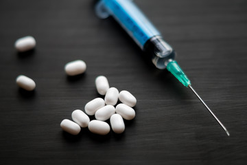 White and green oval pills with syringe on black wooden background.