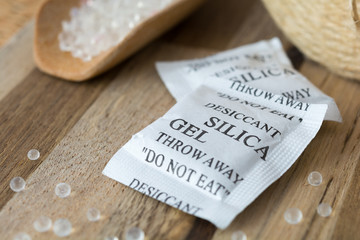 Desiccant or silica gel in white paper packaging and spread on the wooden background. - obrazy, fototapety, plakaty
