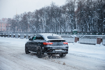 Outdoor view of fast car rides on snowy road on bridge, during cold winter day. Snowfall in city. Vehicle covered with snow. Automobile on frosty road