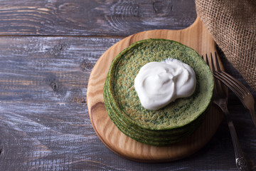 Spinach pancakes with sour cream on a wooden board, rustic style, free space, selective focus