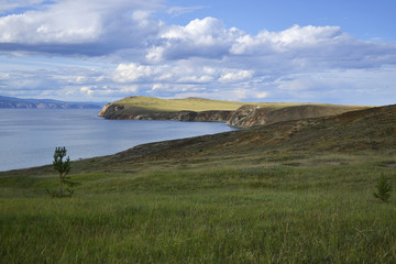 great white cloud green meadow and cape, mountains in the background and the blue water of the...