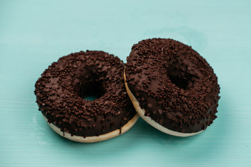 Two chocolate donuts on a turquoise wooden background