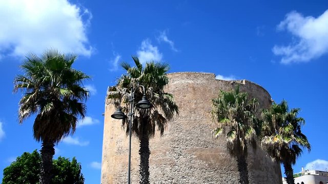 Historic tower and palms under a cloudy sky in Alghero. Sardinia, Italy
