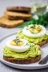 Avocado egg spring toasts on concrete background. Selective focus, close up, space for text.