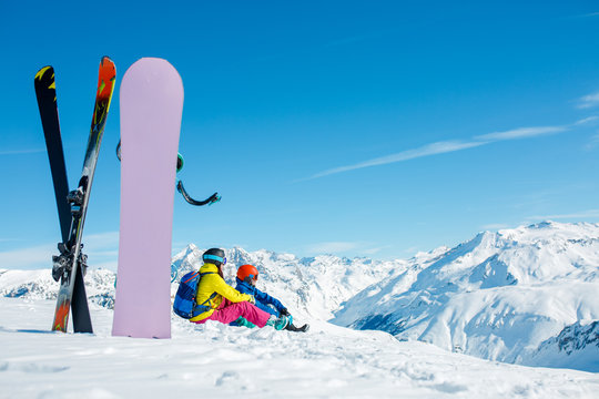 Picture of snowboard, skis on background of sitting sports couple on a snowy hill