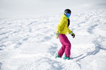 Image of female athlete wearing helmet and mask, snowboarding from snowy mountain slope