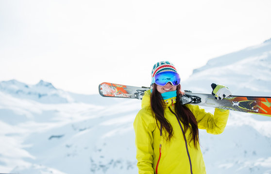 Picture of athlete woman with skis on her shoulder against background of snowy hill