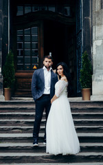 Naklejka premium Full-length wedding shot of the beautiful young newlywed couple posing on the stairs of the old church.
