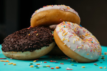 Three donuts, one on top of another, chocolate and white cream on turquoise wooden table