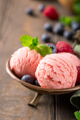 Raspberry ice cream scoops in copper bowl with forest berries and mint decoration. Summer food concept with copy space.