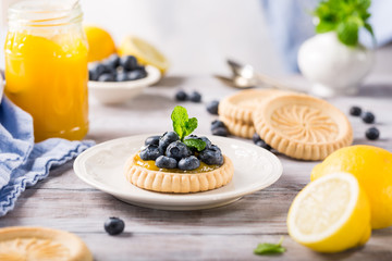 Homemade shortbread tartlet with lemon curd and fresh blueberries on white wooden background. Holiday food concept.