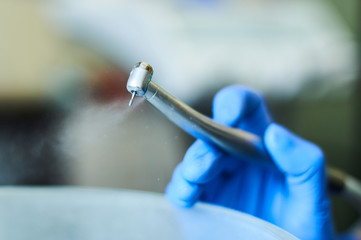 Dentist's hands with blue gloves working with dental drill in dental office.