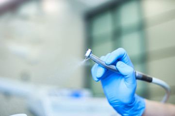 Dentist's hands with blue gloves working with dental drill in dental office.