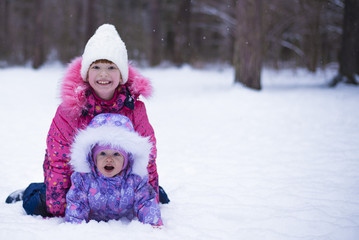 Fototapeta na wymiar Two little girls lying on snow among the winter landscape.