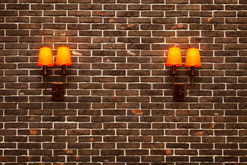 Decorative, neat wall made of brown ceramic clinker bricks and two wall lamps with orange shades.