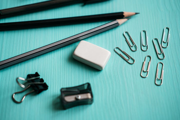 Pen, two pencils, eraser, metal clips on turquoise background