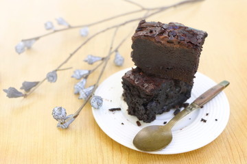 closeup chocolate brownie in white plate on wooden table with beautiful flower, style vintage