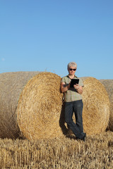 Naklejka na ściany i meble Female farmer examining wheat field with bale after harvest using tablet