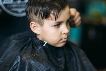 The boy getting haircut by scissor in barbershop. Barber use scissor