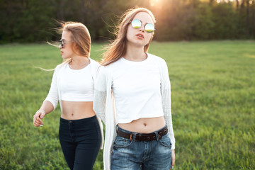 Pretty young females are strolling on the green field in the evening.