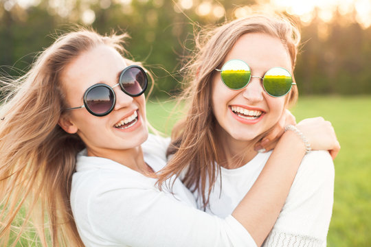 Two women in sunglasses are having a good time on the green field
