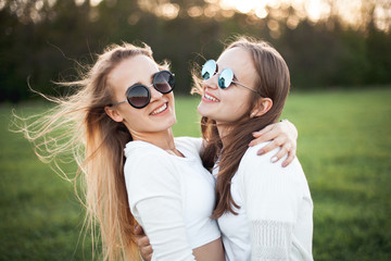 Two beautiful females are hugging on the green field.