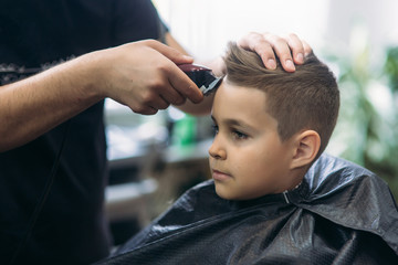 Professional hairdresser uses a hair clipper for fringing hair for a small boy