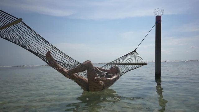 Sexy woman in bikini relaxing in a hammock in the sea under bright blue sky