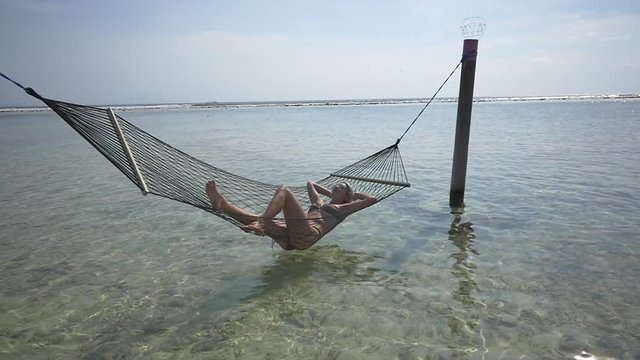 Young woman in bikini relaxing in a hammock above the ocean on a sunny day
