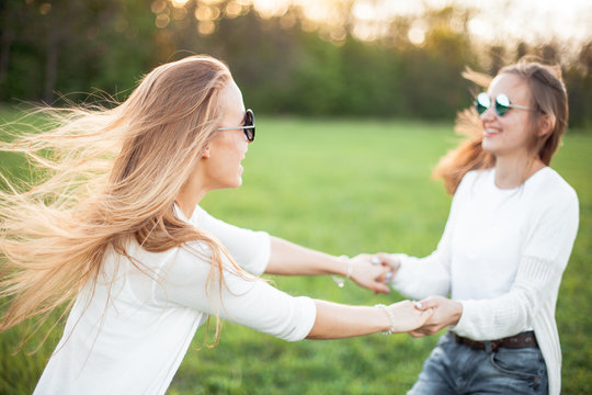Two young females are waving under the sunlight.