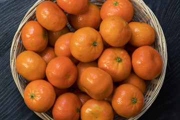Clémentines et leurs feuilles dans une corbeille sur fond noir